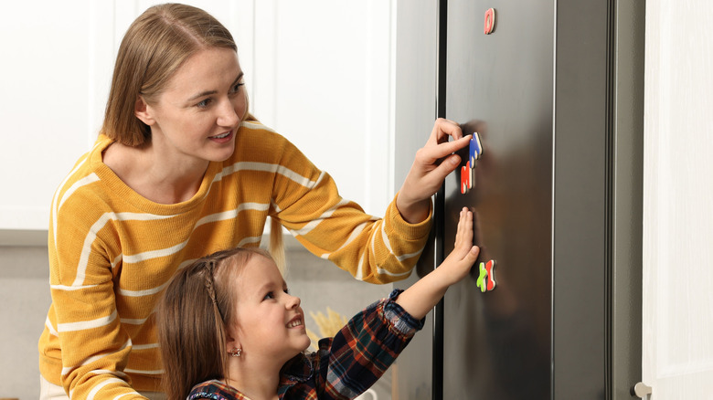 Mother and daughter attaching a magnet to fridge