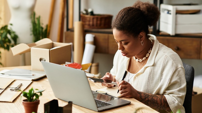 Woman doing purchasing research while on phone and laptop