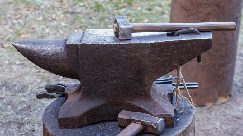 An anvil with hammers and other tools sitting near and next to it
