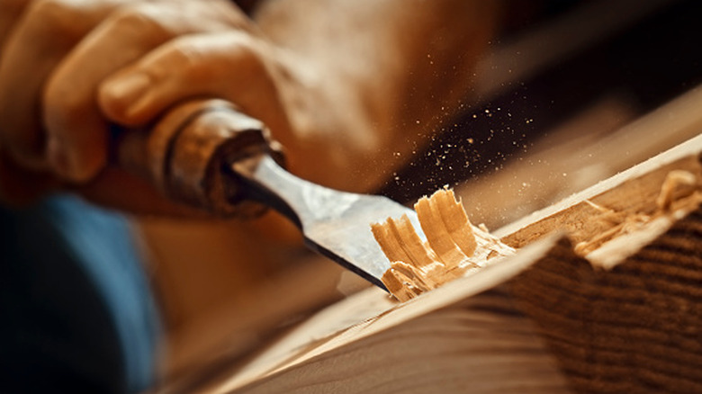 A person using a chisel to carve away bits of wood