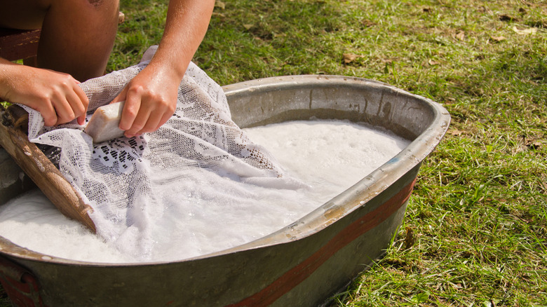 A person washing a piece of lace in a washbasin with a washboard
