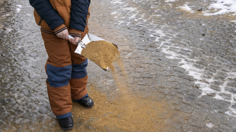 Person scattering sand on an icy street