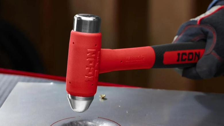 A person uses an Icon 24-ounce ball peen dead blow hammer on a piece of metal