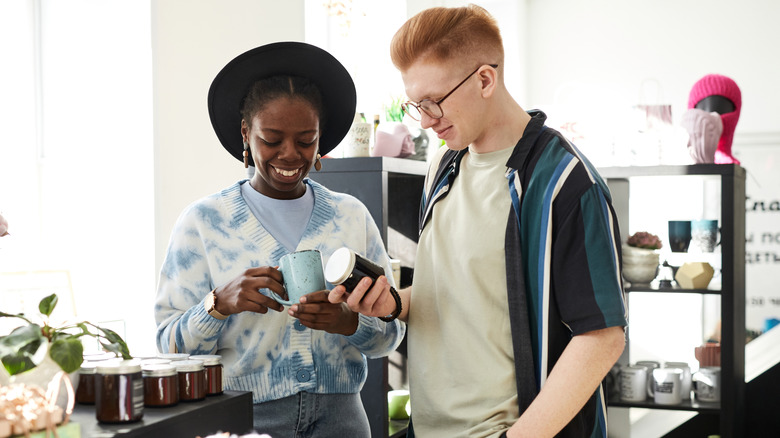 Two smiling young people looking for good deals in thrifting shop or swap event