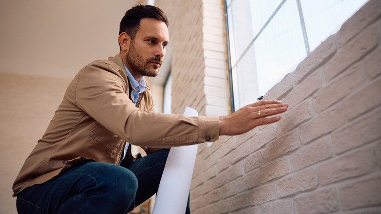 man looking at the brick wall in his home