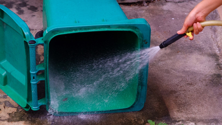 Woman spraying large green trash can with water