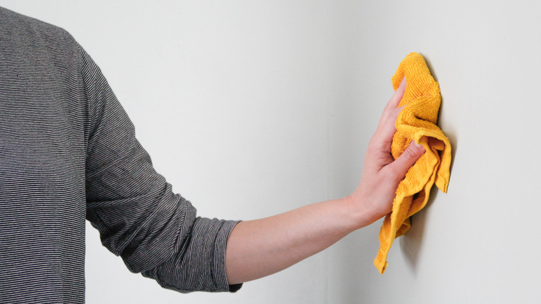 Close up of person wiping down wall with yellow rag