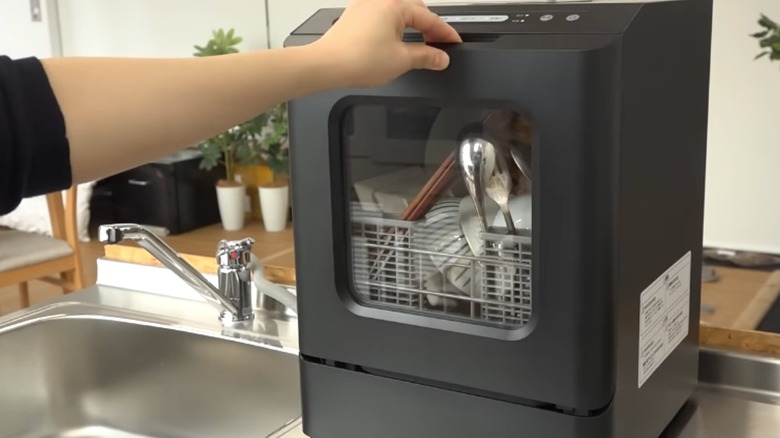 Person opening Thanko mini dishwasher on counter