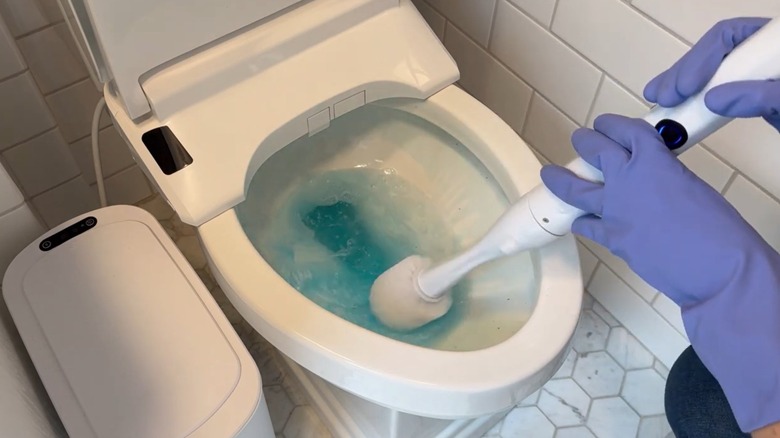 A sleek, white electric toilet brush being used to clean a toilet