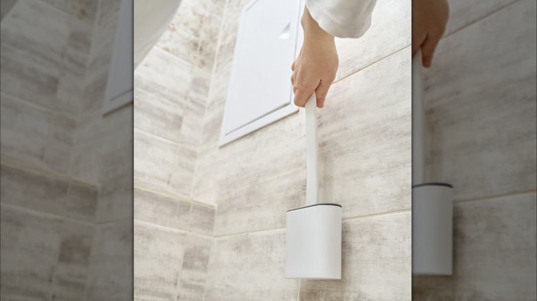 A hand reaching for a mounted toilet brush