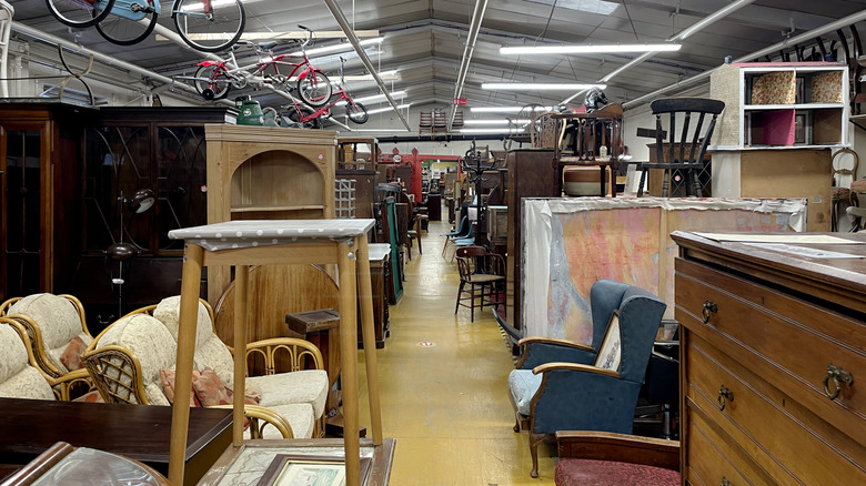 A thrift store furniture aisle with dressers, chairs, and shelving units.