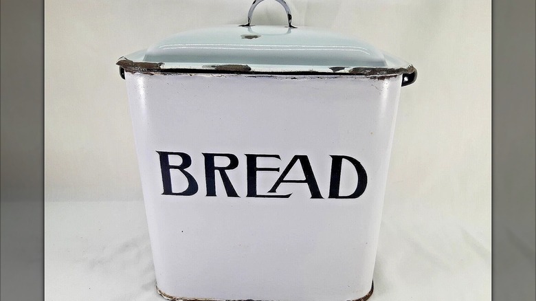A white enamel breadbox with writing on the front.