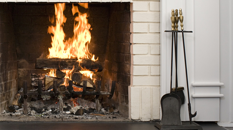 Set of fireplace tools with brass handles next to a flaming fire