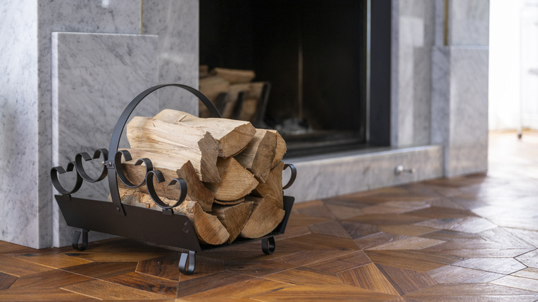 Black metal firewood holder sitting next to marble fireplace