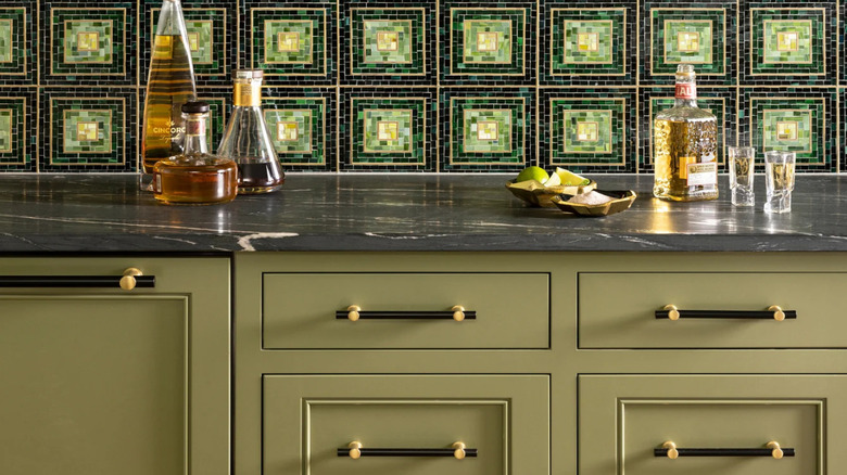Bottles of liquor sit on a marble kitchen countertop in front of a green mosaic patterned backsplash