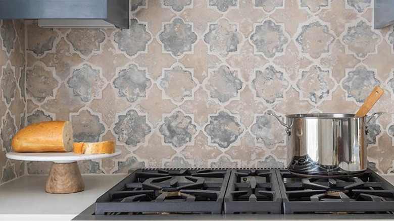 A gas stove sits in front of an earthy arabesque tile backsplash