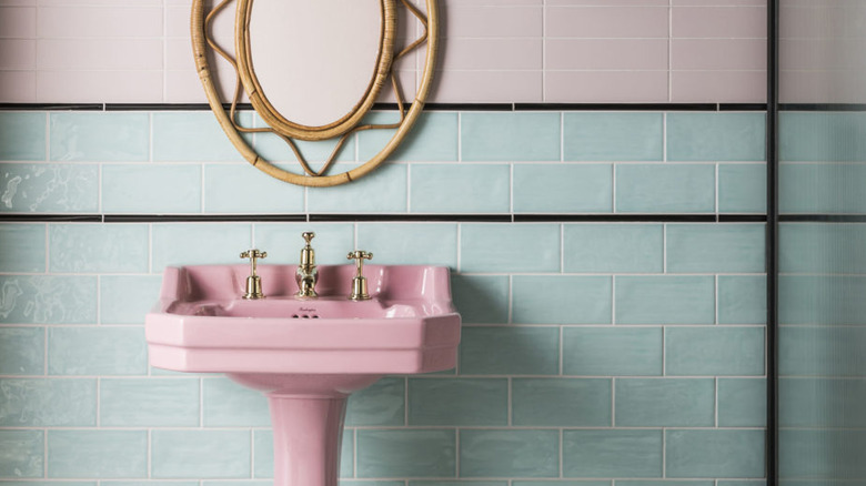 A pink pedestal sink sits in front of a soft blue tile covered wall