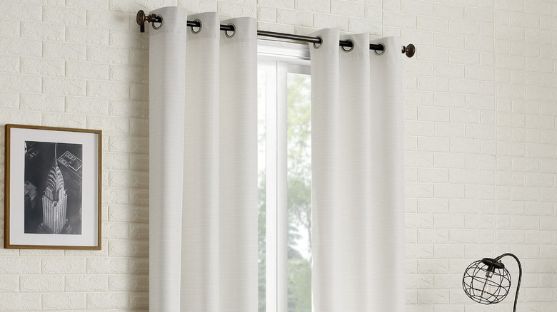 White thermal curtains hanging in a white brick room