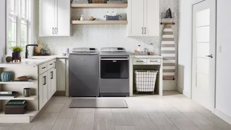 Silver-colored top loading washer and dryer in a spacious laundry room