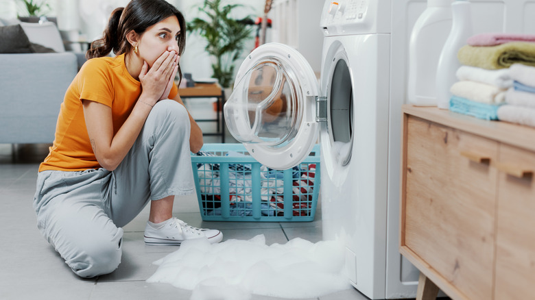 Shocked woman sitting in front of a washer leaking soapy water