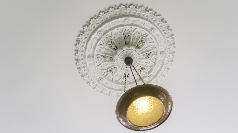 A light fixture hangs from the center of a vintage plaster ceiling medallion