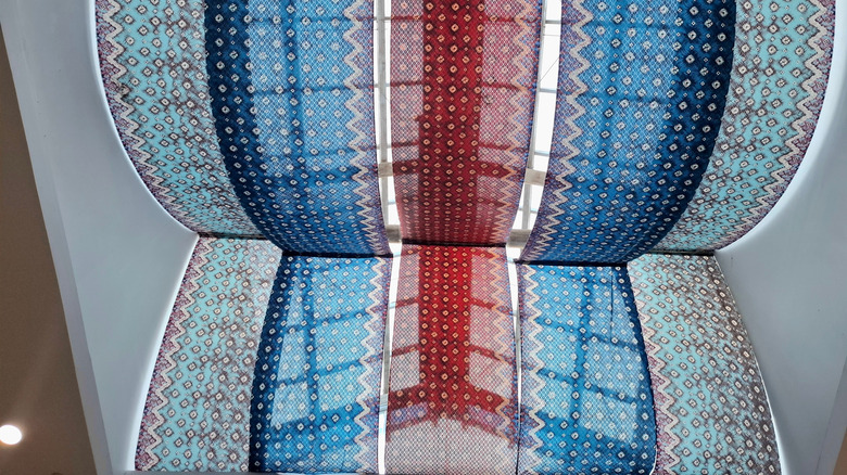 Long colorful pieces of fabric are draped to cover a large ceiling skylight