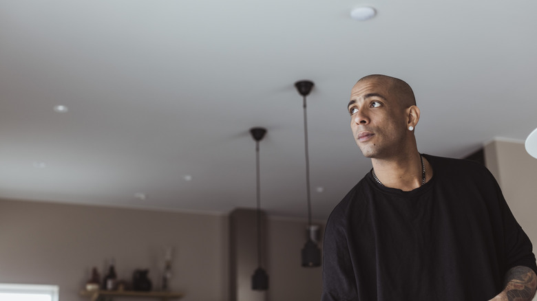 A man looks up toward a plain white ceiling
