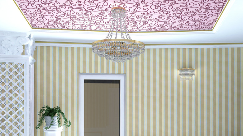 Swirly pink wallpaper is installed on a ceiling above an ornate chandelier