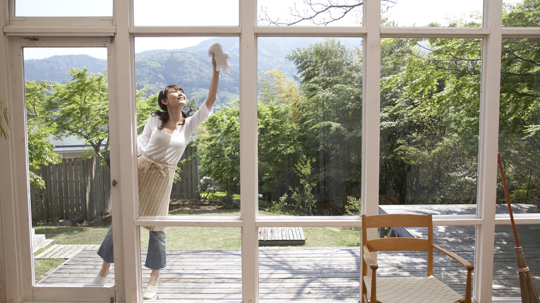 A woman standing on her toes cleaning large windows