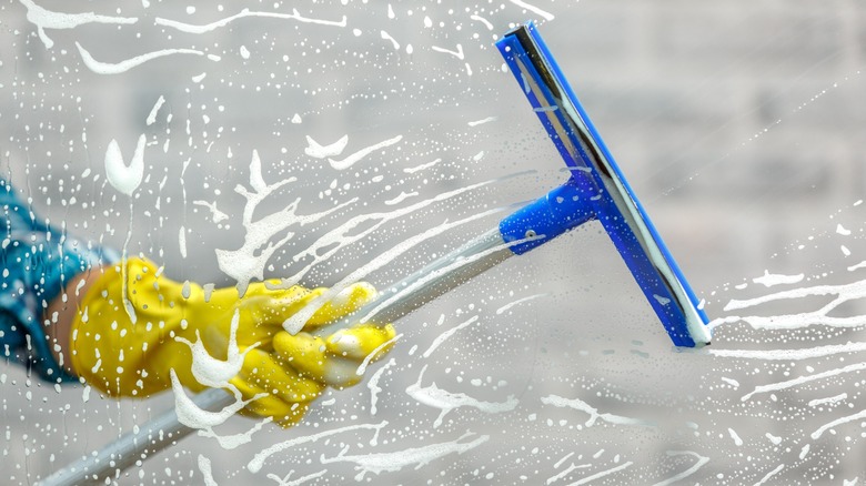 Hand with glove holding squeegee and cleaning a window
