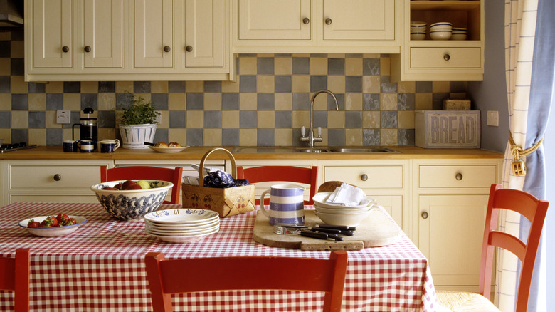 A kitchen with bright red chairs and checkered tablecloth