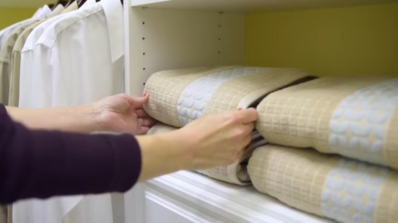 Hands neatly stacking towels in open closet.