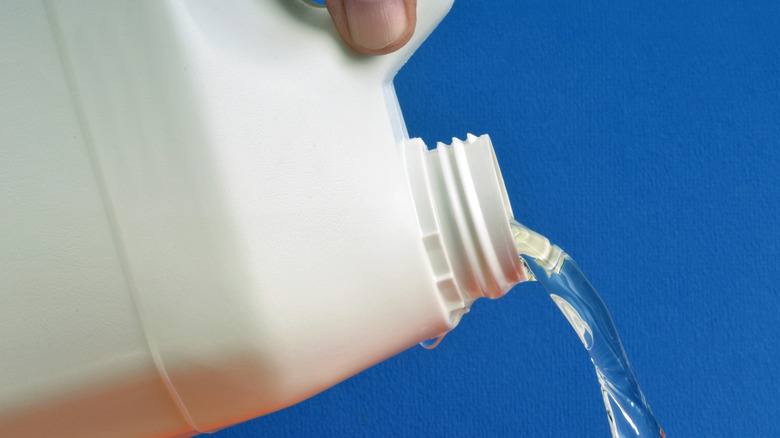 Bleach being poured out of a white container against a blue background