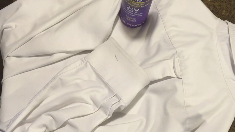 A purple bottle of hairspray on a white shirt
