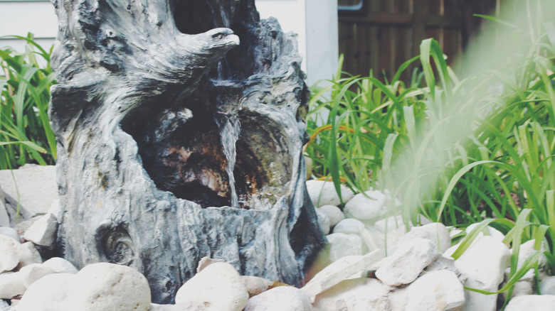 Flowing water in a tree stump surrounded by rocks and ornamental grass