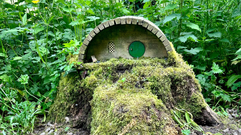 Miniature hobbit home build on a moss covered tree stump in a gard with tall plants