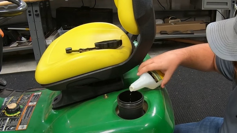 Person adding fuel stabilizer to riding lawn mower