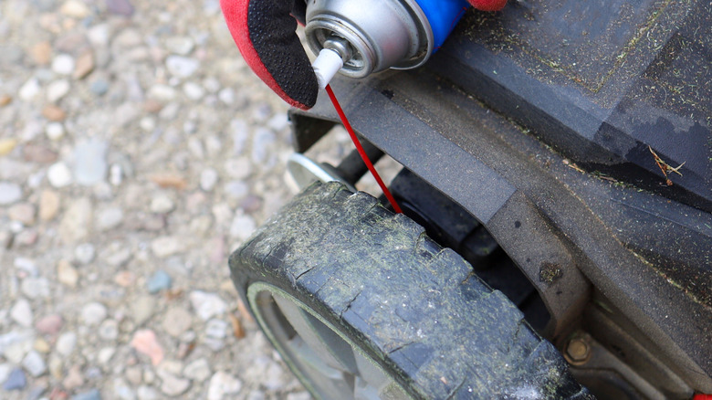 Person spraying WD-40 on lawn mower tire