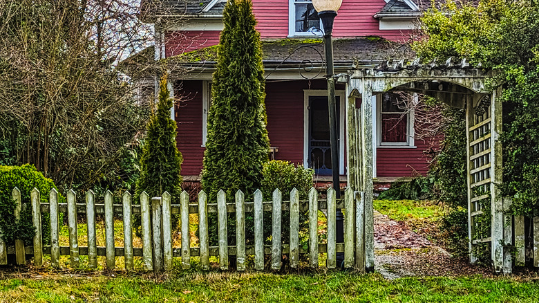 Algae covered picket fencing is in front of an old house