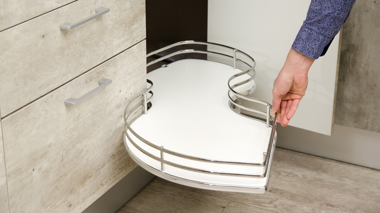 A man pulling a swing-out tray out from a corner cupboard