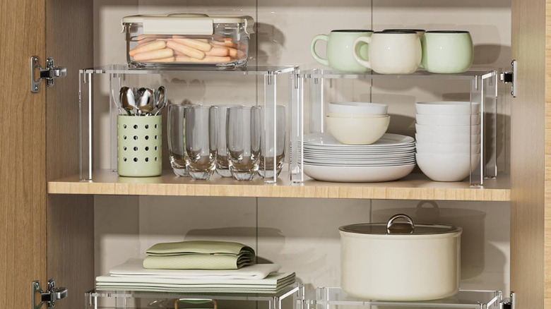Clear plastic shelf risers in a kitchen cupboard