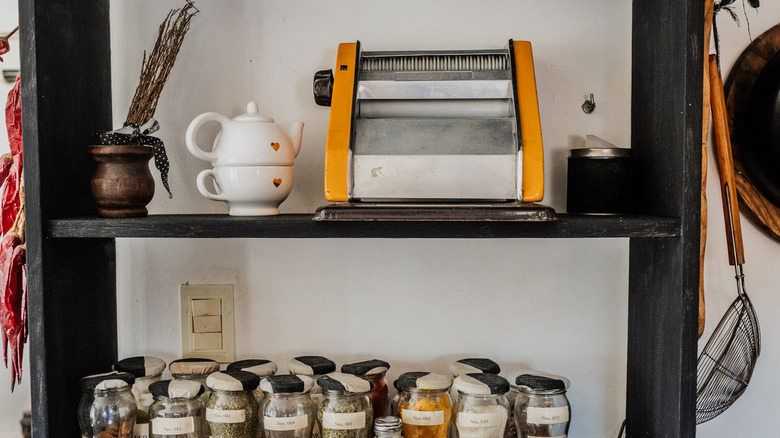 A kitchen shelf with various ingredients on it, plus an old-fashioned pasta roller