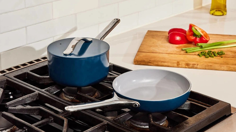 Small blue frying pan and pot on stovetop beside prepped food on cutting board