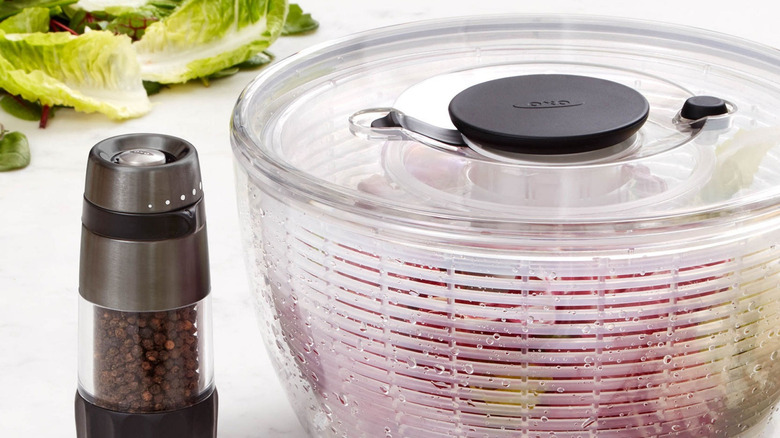 Plastic salad spinner beside peppercorn grinder on white countertop