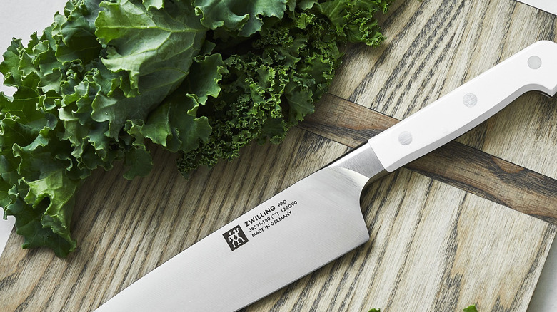 Solid steel chef's knife with white handle on rustic wood cutting board