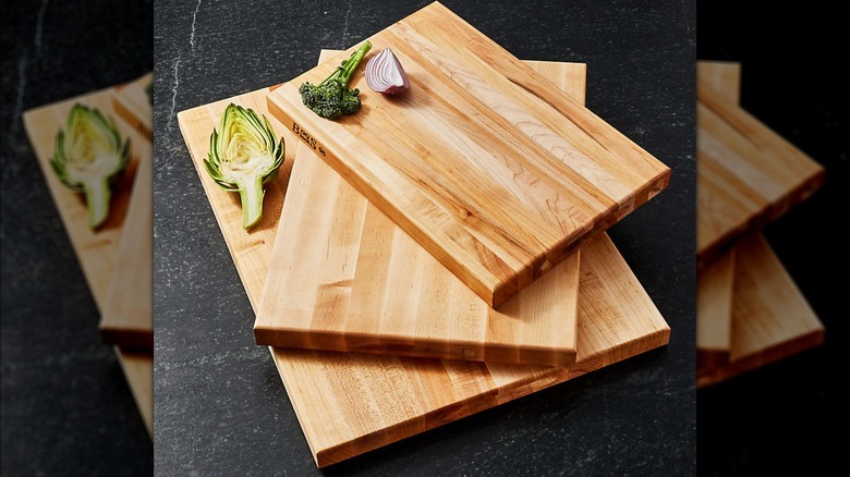 Pile of maple wood cutting boards on black stone kitchen counter with ingredients