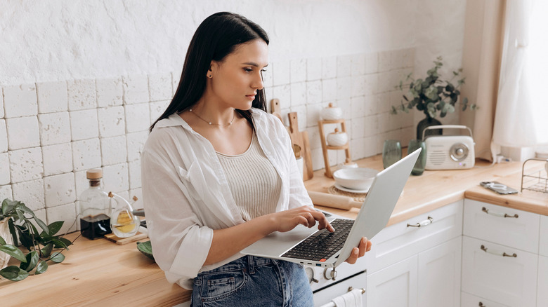 Young woman seriously browsing laptop in bright, contemporary kitchen