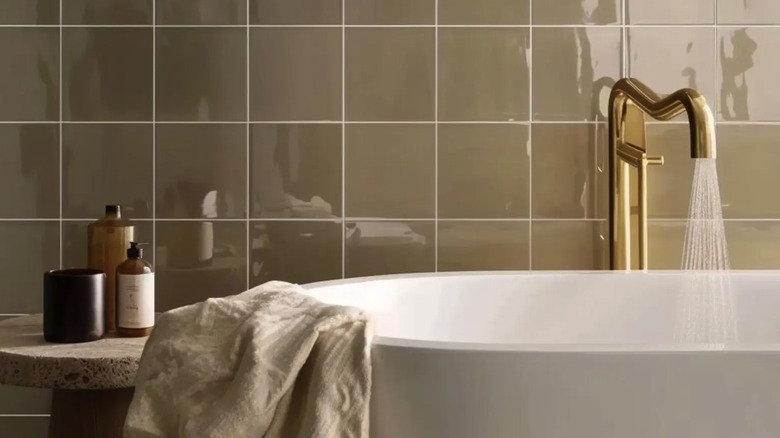 A bathroom with a zellige tile wall and a large tub with a gold faucet.