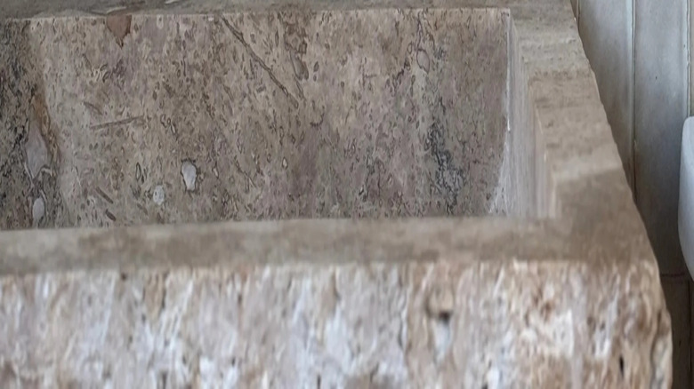 A limestone sink with a white zellige tile backsplash and soft gold faucet.