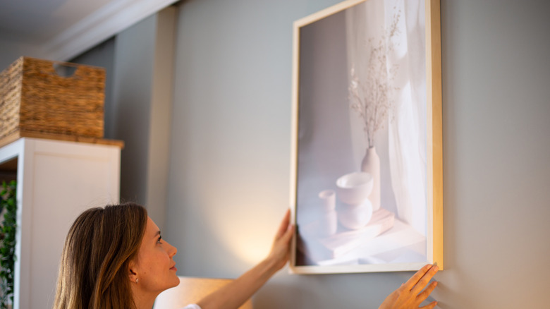 A woman hanging a framed photo of a vase